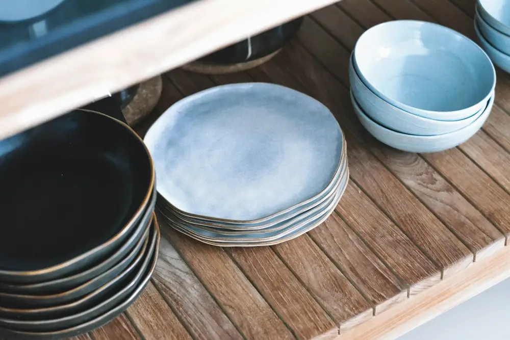 Stacks of pale blue and dark glazed plates on a wooden shelf